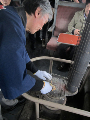 A conductor on board the train moves quickly to cook dried surume squid on the grill of the dharma stove.